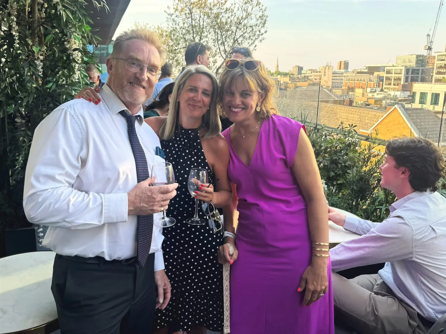 Three members with drinks on the terrace, the City skyline behind them